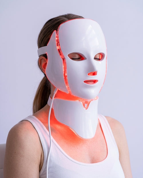 Mujer con la mascarilla LED Dermiq y la pieza del cuello encendidas en luz roja, primer plano de la cara